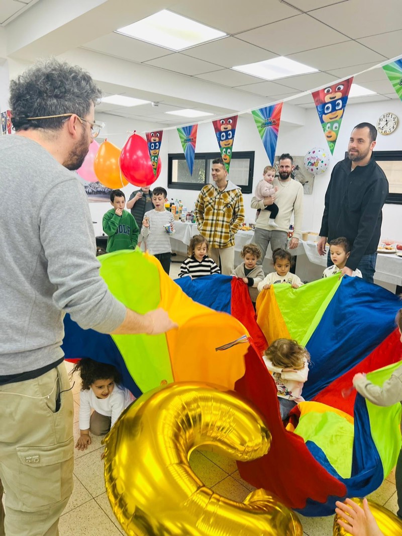 אבות משתתפים עם ילדים במשחק מצנח צבעוני - גם ההורים חלק מהכיף